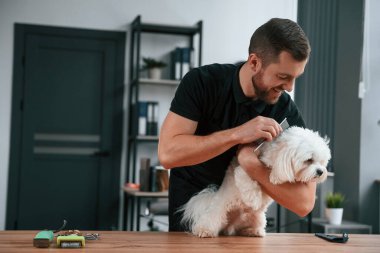 Hayvanlar masada. Groomer içeride Maltalı köpekle birlikte. Siyah üniformalı adam..