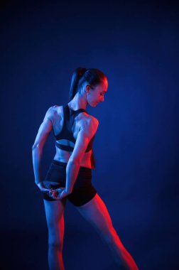 Arkadan bak. Gerinme egzersizlerini ısıt. Güzel kaslı kadın stüdyoda neon ışıklı..