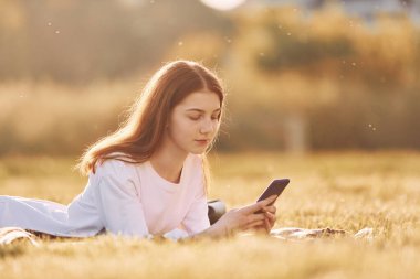 Akıllı telefon ellerindeyken. Genç kız güneşli bir günde sahada güzel bir hafta sonu geçiriyor..