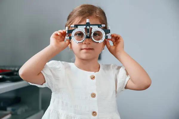 stock image Looking forward with special device on the eyes. Little girl checking her vision by using special optometrist device.