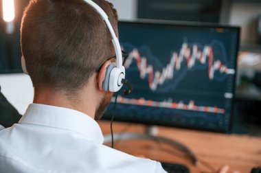 Borsa grafikleri ekranda. Resmi kıyafetli adam modern ofiste çalışıyor. Bilgisayar kullanılıyor.