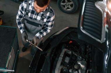 Aletleri kullanmak ve arabayı tamir etmek. Üniformalı adam araba galerisinde çalışıyor..