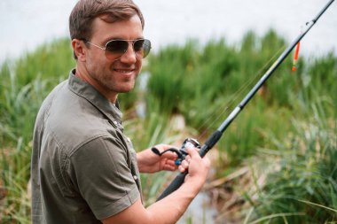 Güneş gözlüklü olumlu ve yakışıklı adam dışarıda balık tutuyor..