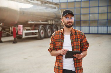 Güneşli bir gün, yakıt tankerine karşı durmak. Gündelik giysiler içindeki genç kamyon şoförü..