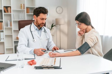 Tansiyon ölçümü. Bir kadınla. Resmi kıyafetli doktor dolapta çalışıyor..