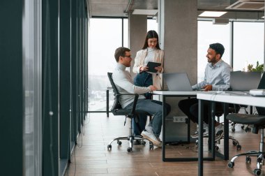 Gülümsüyor ve konuşuyor. Erkekler ve kadınlar ofiste birlikte çalışıyorlar..