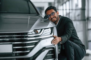 Ulaşımı kucaklıyorum. Takım elbiseli yakışıklı Hintli adam araba galerisinde araçla birlikte..