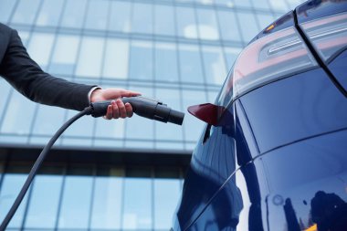 Manzarayı kapat, şarj aletini prize tak. İş adamı dışarıda elektrikli arabasının yanında duruyor..