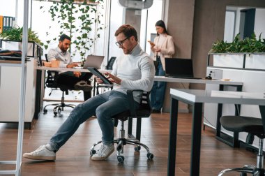 Tabletle birlikte sandalyede. Erkekler ve kadınlar ofiste birlikte çalışıyorlar..