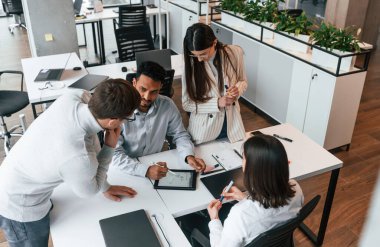 Masanın yanında. Ofiste birlikte çalışan dört kişi var..