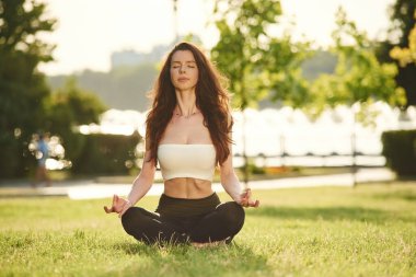 Lotus pozunda meditasyon. Spor elbiseli güzel bir kadın güneşli bir günde parkta..