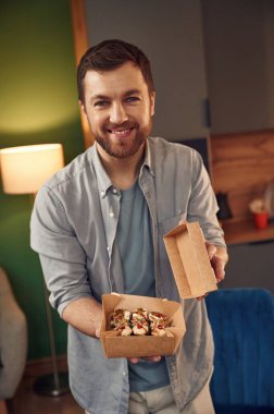 Yakışıklı adammış. Günlük kıyafetli adam elinde kağıt eko kutudaki suşiyi tutuyor..