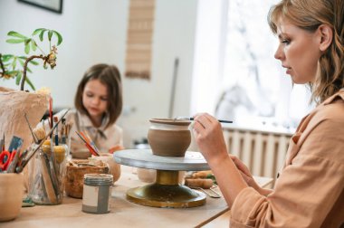 Anne ve küçük kız atölyede seramik demlik yapıyorlar..