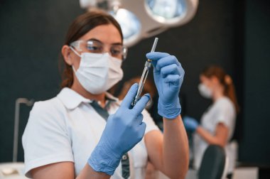 Mavi parlayan doktor ayakta ve ekipmanları tutuyor. Stomatolojik dolapta..