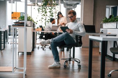 Dijital cihazla sandalyede oturan kişinin arkasından konuşmak. Erkekler ve kadınlar ofiste birlikte çalışıyorlar..