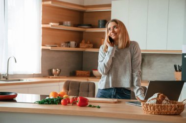Ayakta dikilip telefonla konuşuyor. Güzel genç bayan mutfakta..