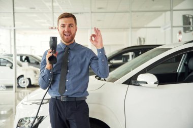 Şarj aleti ile eğleniyorum. Yakışıklı araba galerisi çalışanı elektrikli araçla çalışıyor..