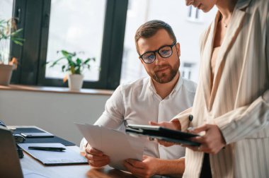 Kadının elinde tablet var, bilgiyi analiz ediyor. Modern ofiste iki çalışan birlikte çalışıyor..