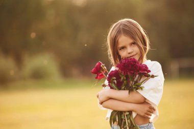 Güzel kırmızı çiçekler tutuyordu. Küçük kız gündüz vakti yaz tarlasında..