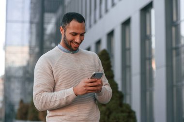Yürüyorum, akıllı telefon tutuyorum. Yakışıklı siyah adam iş binasının yakınında dışarıda..