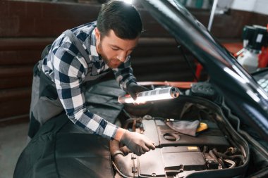 Kaputun altında. Işıklandırma ekipmanlarını tutmak ve arabanın sorunlarını çözmek. Üniformalı adam araba galerisinde çalışıyor..