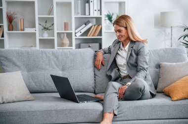 Resmi elbiseli kadın evde, kanepede oturuyor..