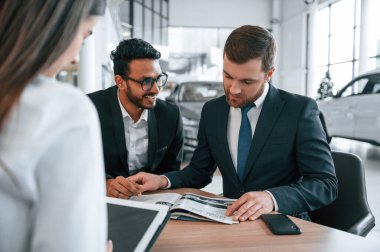 Otomobili seçiyorum. Araba galerisinde üç kişi birlikte çalışıyor..