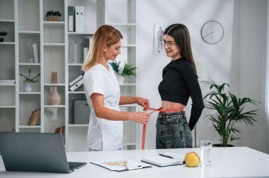 Diyet yapma, kilo alma, bel ölçme. Beslenme uzmanının randevusundaki genç bir kadın. Tıbbi bakım.