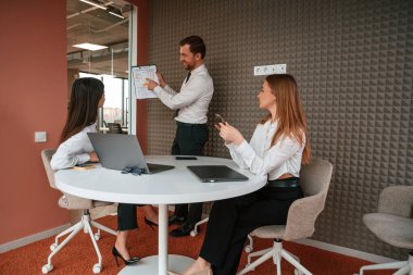 Yönetici plan projesini gösteriyor. Ofiste üç iş adamı birlikte çalışıyor..