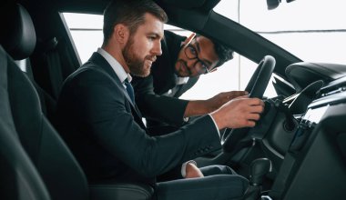 Otomobilin içini müşteriye gösteren adam.