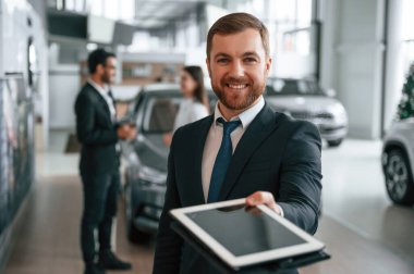 Grafik tablet kullanarak. Araba galerisinde üç kişi birlikte çalışıyor..