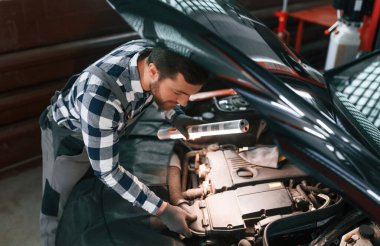 Kaputun altında. Işıklandırma ekipmanlarını tutmak ve arabanın sorunlarını çözmek. Üniformalı adam araba galerisinde çalışıyor..