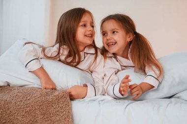 Gülümsüyor, yatağa uzanıyor. İki küçük kız evcil odada oynuyorlar ve eğleniyorlar..