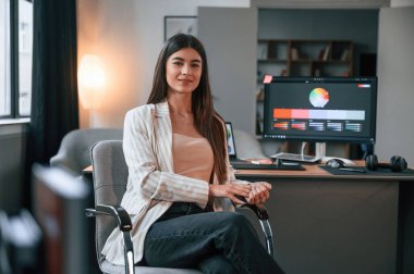 Sandalyede otururken. Tasarımcının yazılımı ekranda. Kadın modern ofiste bilgisayarla çalışıyor..