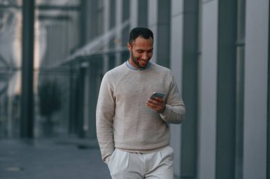 Yakışıklı adam yürüyor, elinde akıllı telefon var. Dışarıda, iş binasının yanında..