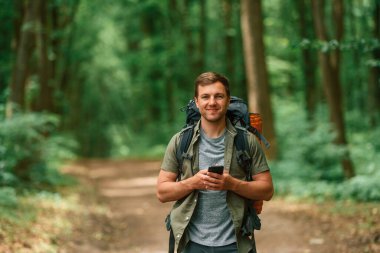 Büyük bir sırt çantası ve akıllı telefon. Yaz ormanında bir turist. Keşif ve eğlence kavramı.