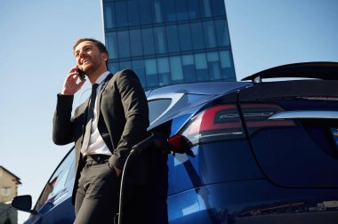 İş görüşmesi, telefonla konuşmak. Adam dışarıda elektrikli arabasının yanında duruyor..