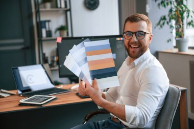 Tasarımcı proje için farklı renkler seçiyor. Resmi kıyafetli adam modern ofiste çalışıyor. Bilgisayar kullanılıyor.