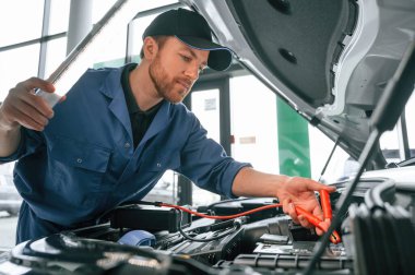 Elektrik terminallerini kullanarak bozulmayı test etmek. Mavi üniformalı adam araba servisinde çalışıyor..