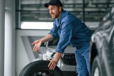Lastiği hareket ettiriyorum. Mavi üniformalı adam araba servisinde çalışıyor..