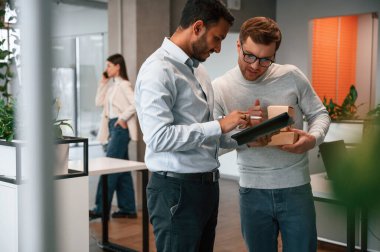 Men are holding tablet and paper eco boxes. Business people are working together in the office. clipart