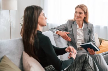 İki kadın kanepede oturuyor ve konuşuyor. Sıradan ve resmi kıyafetler..