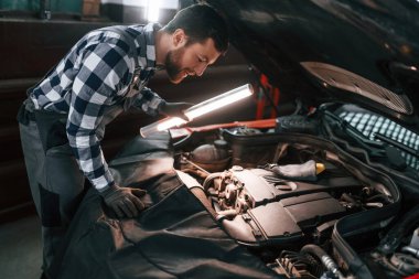 Kaputun altında. Işıklandırma ekipmanlarını tutmak ve arabanın sorunlarını çözmek. Üniformalı adam araba galerisinde çalışıyor..