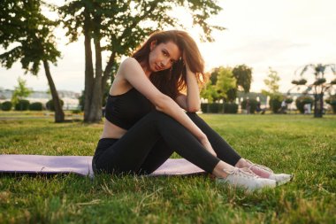 Yoga minderinde güneş ışığına karşı oturmak. Spor elbiseli güzel bir kadın güneşli bir günde parkta..