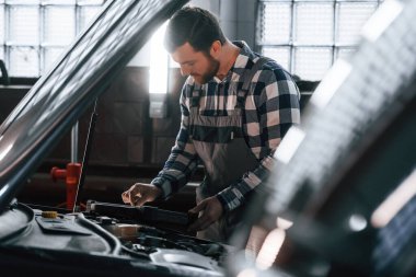 Arabanın kaputu açıldı. Tablet kullanıyorum. Üniformalı adam araba galerisinde çalışıyor..