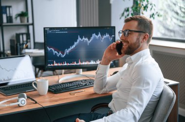 Borsa grafikleri ekranda. Resmi kıyafetli adam modern ofiste çalışıyor. Bilgisayar kullanılıyor.