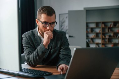 Takım elbiseli iş adamı bilgisayarla ofiste..