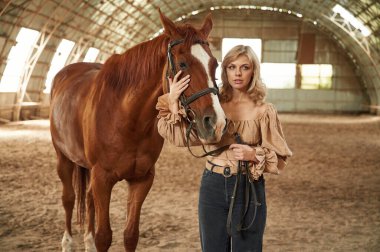 Kotlar ve krem renkli giysiler içinde. Güzel genç bir kadın atıyla içeride..
