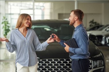 Anahtarları veriyorum. Resmi elbiseli adam elektrikli arabalı kadın müşteriyle birlikte..