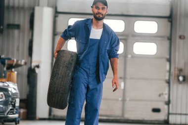 Ön manzara, ayakta ve lastik tutuyor. Otomobil tamircisi garajda çalışıyor. Onarım servisi.